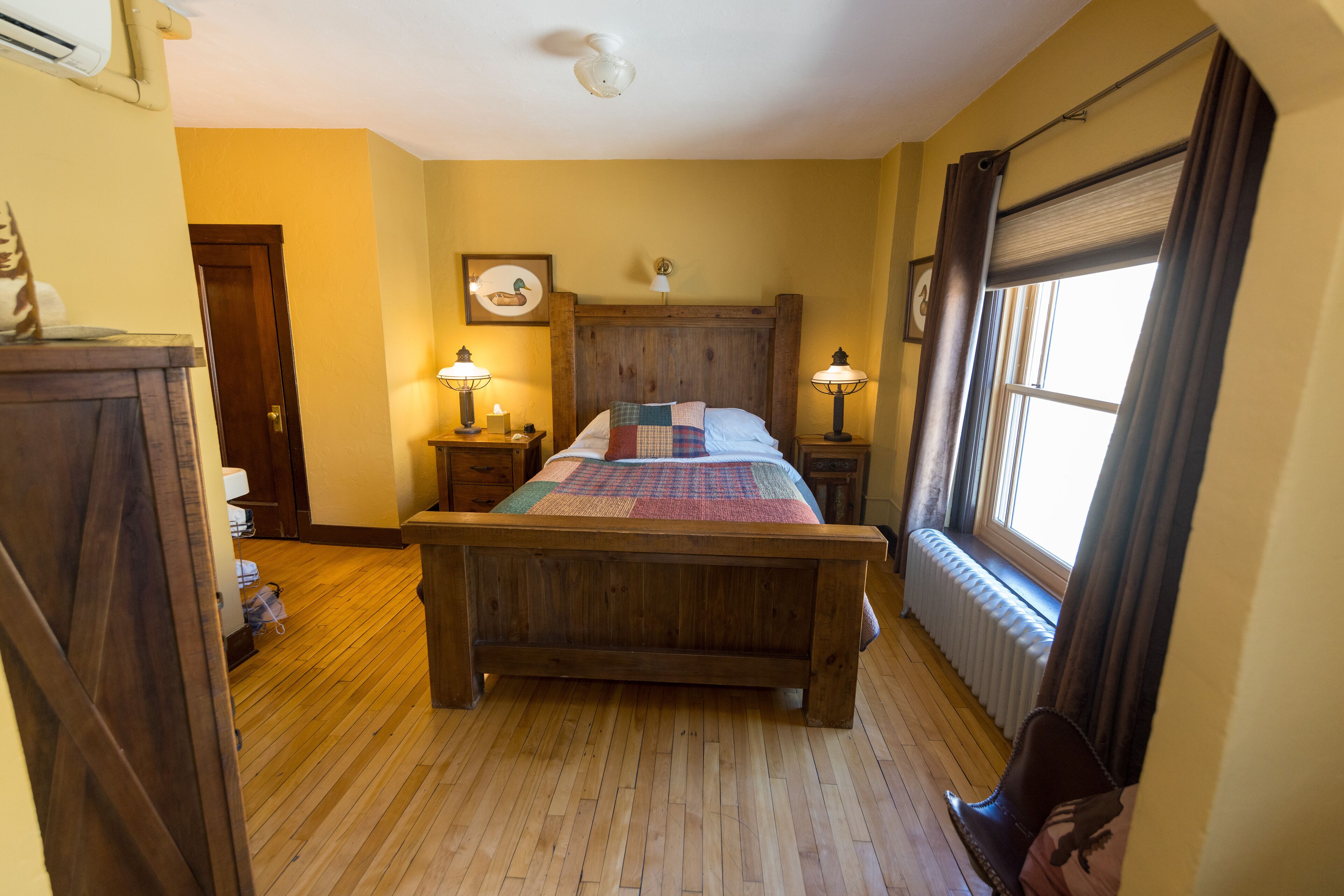 Une chambre à coucher avec un lit en bois, deux lampes de chevet, un radiateur et une fenêtre avec des rideaux.