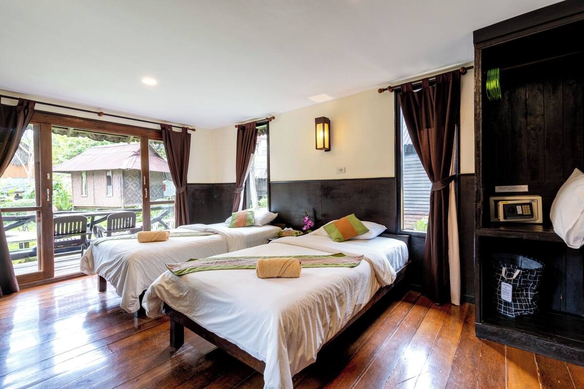 A hotel room with two beds, a wooden floor, a large window, and a view of the outside.