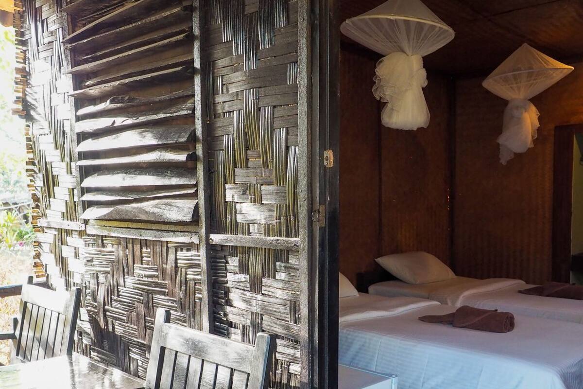 A room with a bed, a wooden chair, a table, and a woven partition.