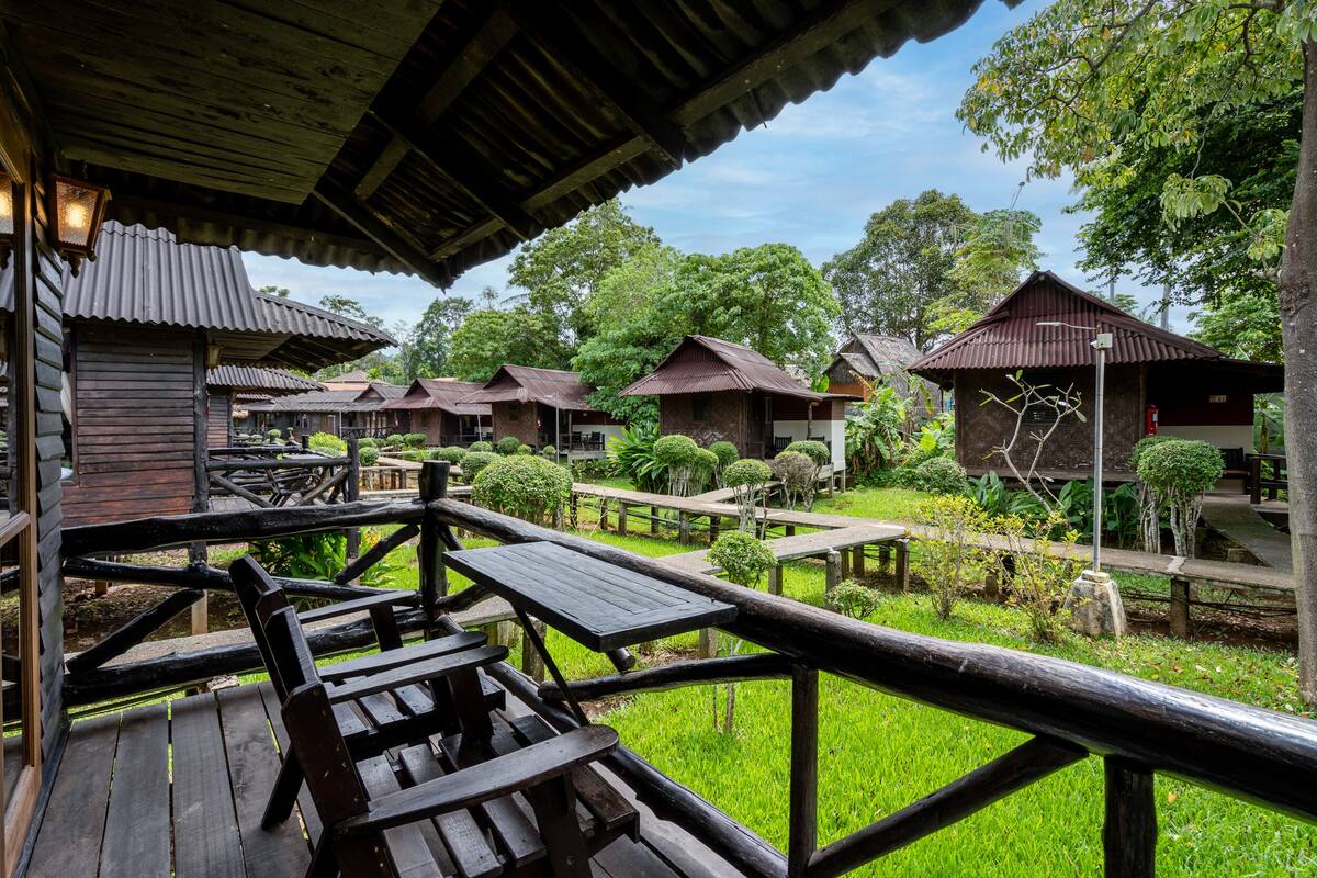 A wooden deck with benches and a view of several rustic-style cabins surrounded by lush greenery.