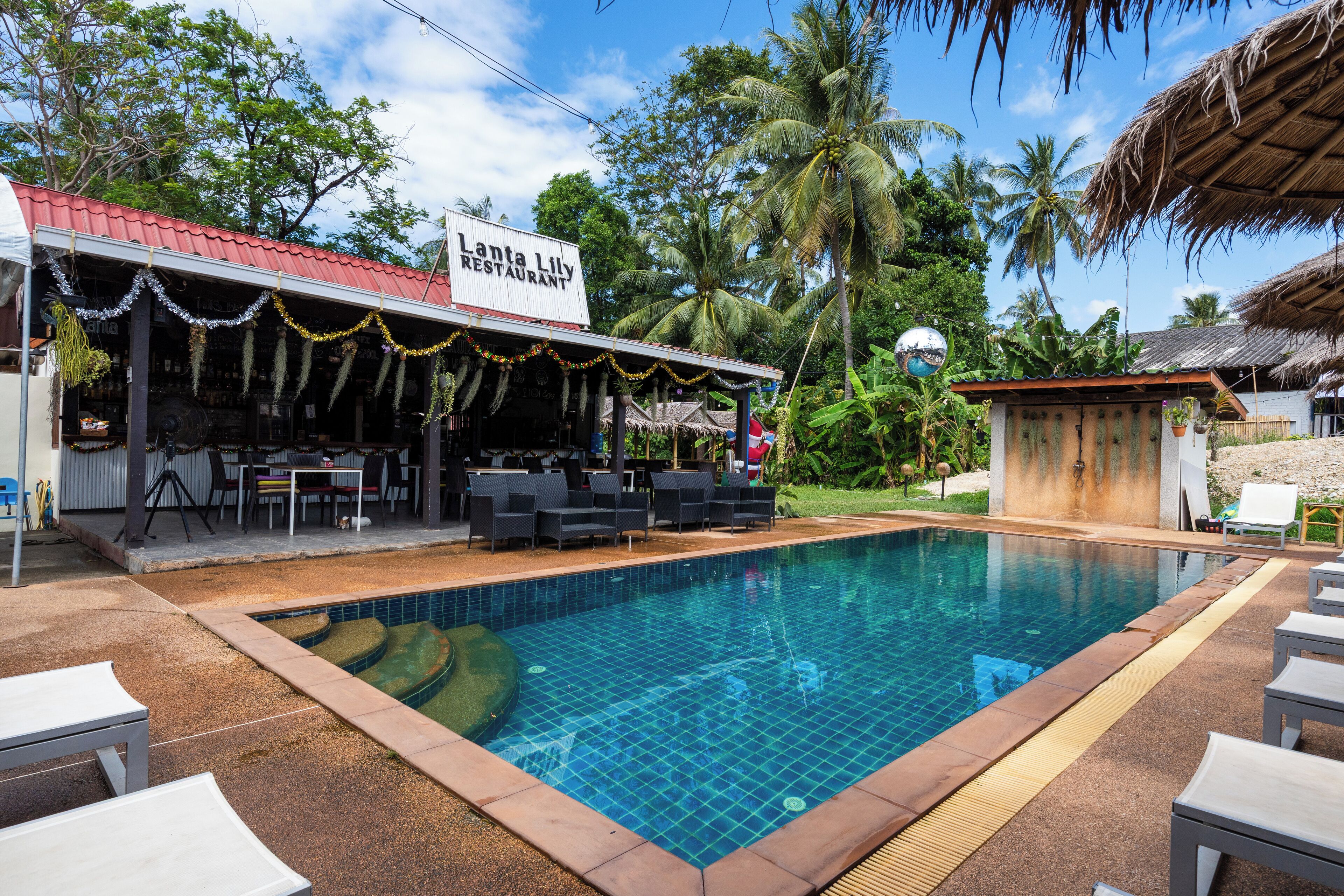 A swimming pool with lounge chairs, a restaurant named 'Lanta Lily Restaurant', and tropical vegetation.