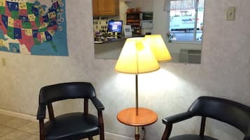 Una habitación con dos sillones de cuero negro, una mesa de madera, una lámpara, un mapa en la pared y una ventana con vista a un camión de reparto.