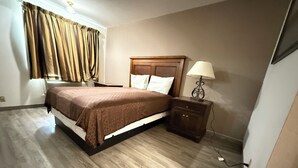 A bedroom with a wooden bed, a nightstand with a lamp, and a window with curtains. - Island Inn (Grand Island)