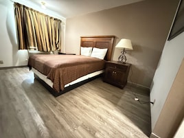 A bedroom with a wooden bed, a nightstand with a lamp, and a window with curtains.