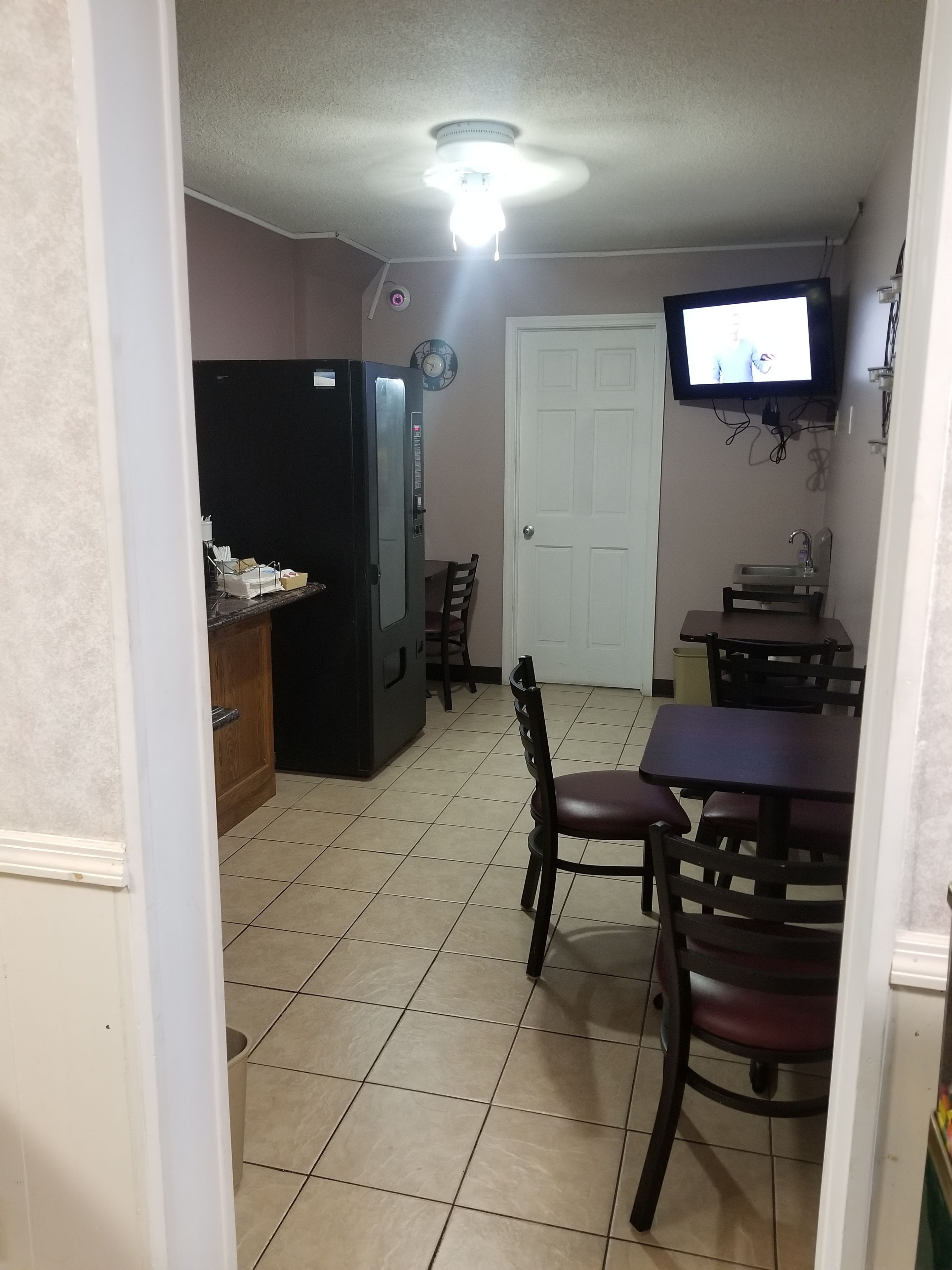 A compact kitchen with a refrigerator, a dining table, and a TV mounted on the wall.