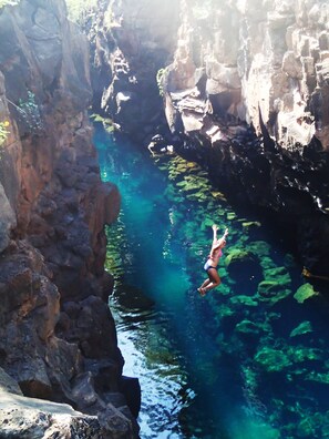 A person diving into a clear blue pool surrounded by rocky cliffs.