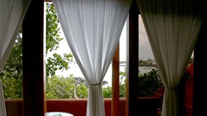A room with a view of a body of water, a small round table, and a red cushioned bench.