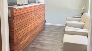 Un espace d’accueil comprenant un comptoir en bois, un bureau et un coin salon avec deux chaises.