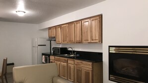 Une cuisine compacte avec des meubles en bois, un plan de travail noir, un four à micro-ondes et une cheminée intégrée.
