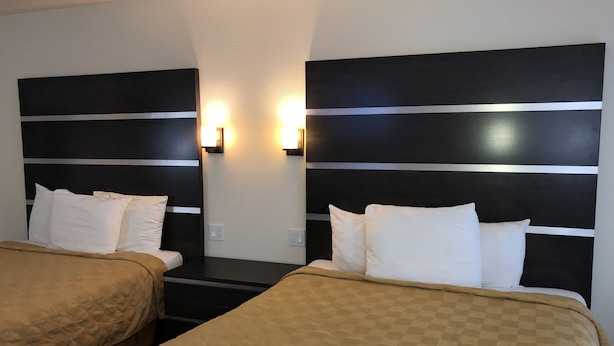 Une chambre d’hôtel avec deux lits, chacun doté d’une tête de lit ornée de rayures horizontales. Des lampes murales sont fixées au-dessus des lits, et les murs sont peints dans un décor bicolore.