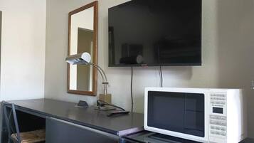 A kitchenette with a microwave, a small table, a lamp, and a TV mounted on the wall.