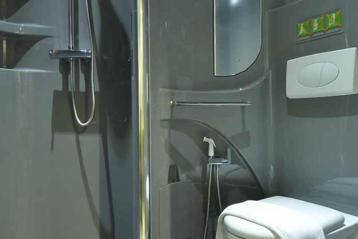 Une salle de bain moderne avec une douche à parois de verre, des toilettes blanches et un panneau de commande visible.