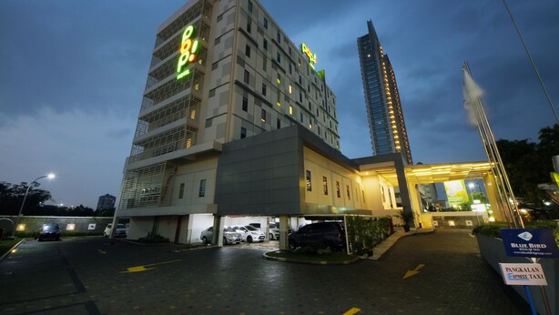 A hotel with a modern design, featuring a prominent 'P! Hotel' sign, a parking area with several cars, and a 'Blue Bird Express Taxi' sign indicating a taxi service.