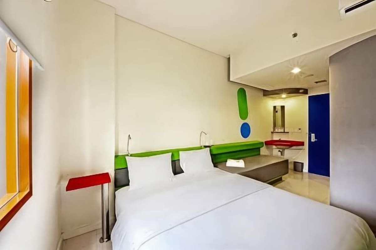Une chambre d’hôtel comprenant un lit, un bureau, une chaise, un miroir et une salle de bain avec un lavabo et des toilettes.