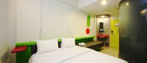 A modern hotel room with a bed, a green and red bedside table, a small sink, and a mirror.