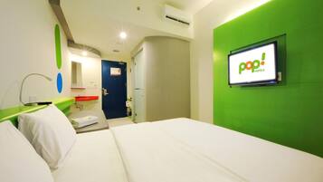 Quarto de hotel com cama, parede de destaque verde, TV exibindo 'pop! HOTELS' e porta que dá para outro cômodo.