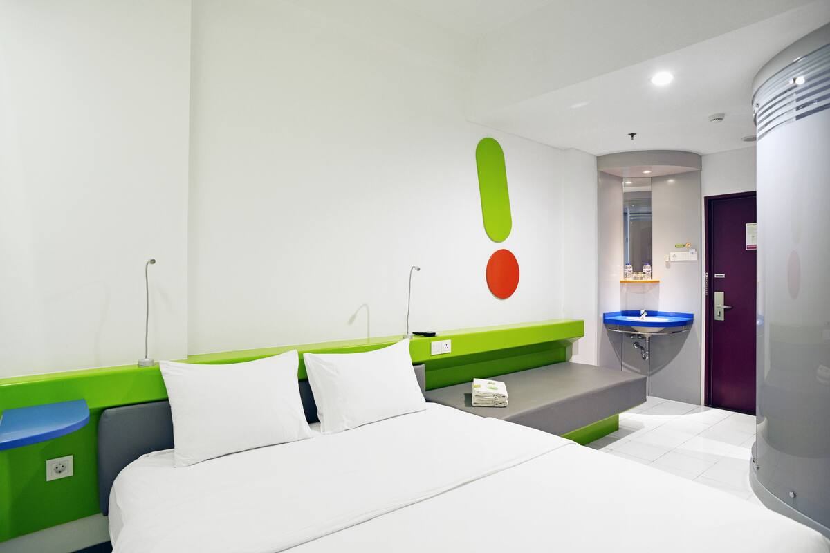 Ein Hotelzimmer mit einem Bett, einem grünen Nachttisch, einem blauen Waschbecken und einer violetten Tür.