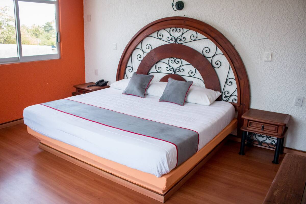 Ein ordentlich bezogenes Bett mit Holz Kopfteil, einem Nachttisch und einem Beistelltisch.