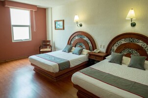 A hotel room with two beds, a chair, a nightstand, and a wall-mounted lamp.