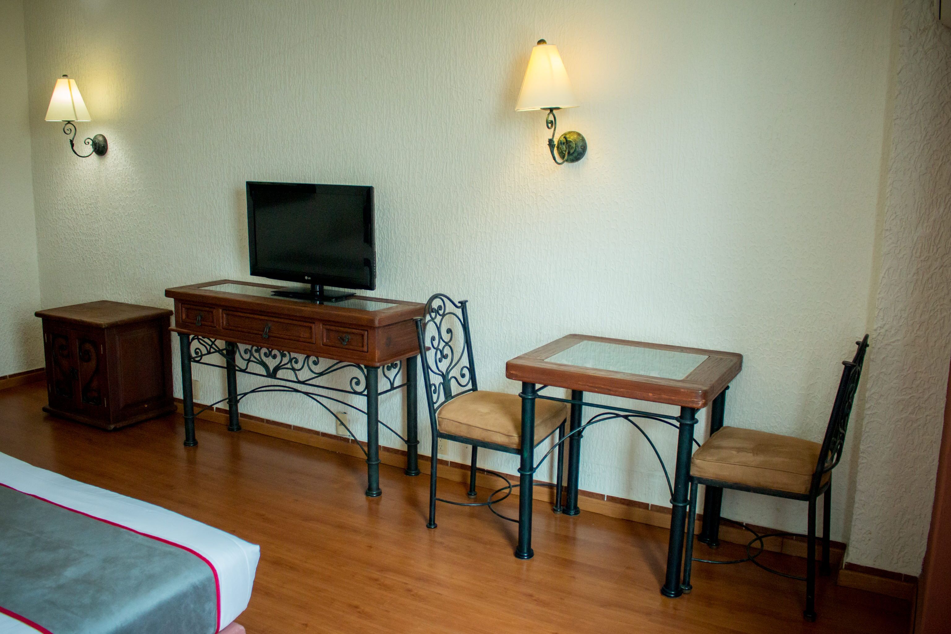 A room with a wooden desk, a television, two chairs, and a small cabinet.