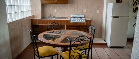 A kitchen with a round table, chairs, a stove, a sink, and cabinets.