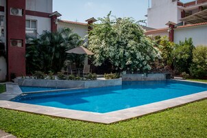 A swimming pool surrounded by a well-maintained garden with a variety of plants and a patio area with chairs.
