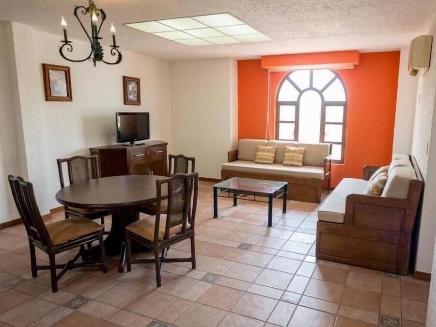 Ein Wohnzimmer mit Essbereich, einem Fernseher und einem Fenster mit orangefarbenen Vorhängen.