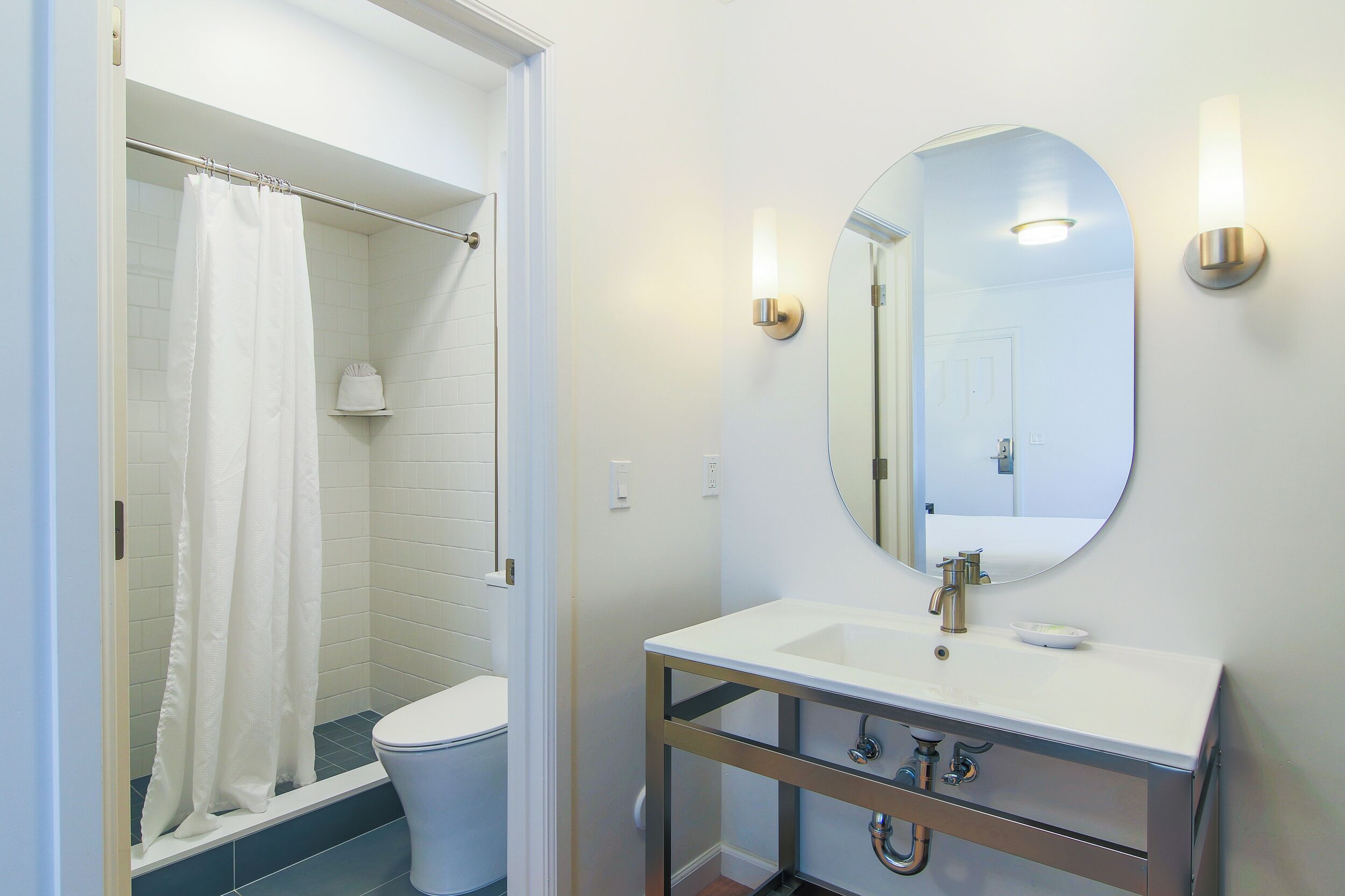 A bathroom with a shower, toilet, sink, and mirror.
