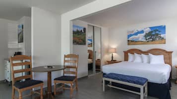 A hotel room with a bed, a desk with chairs, a small table, and a painting on the wall.
