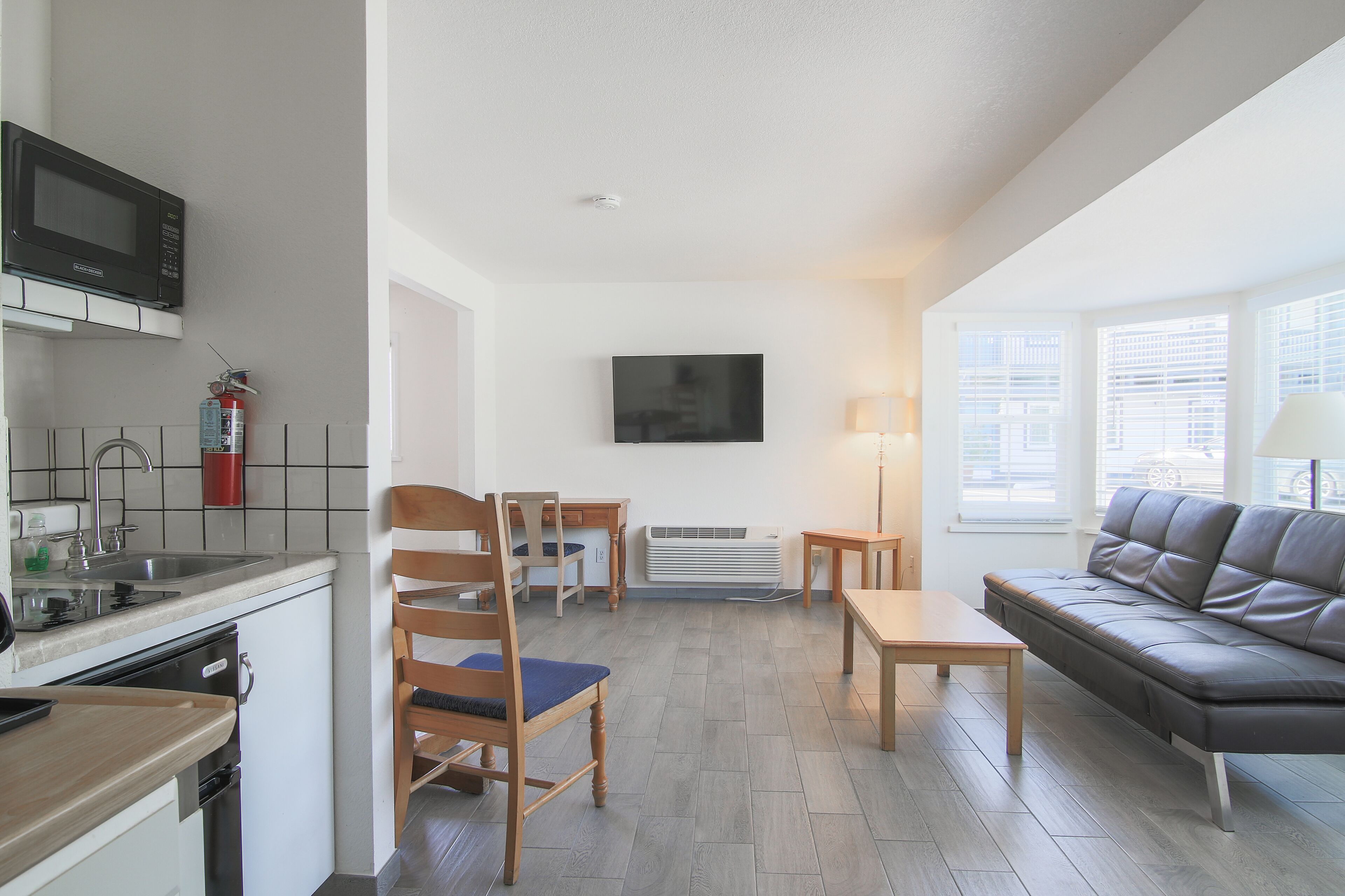A modern living room with a sofa, a TV, a dining table, and a kitchen area with a microwave and sink.