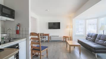 Una sala de estar moderna con sofá, televisor, mesa de comedor y una zona de cocina con microondas y fregadero.