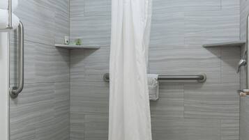A shower area with a white shower curtain, grab bars, and a small shelf with toiletries.