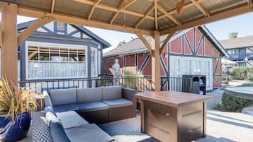 Ein Sitzbereich im Freien mit einer Couch und einem Tisch, eine überdachte Terrasse und Blick auf ein Gebäude mit Garage.