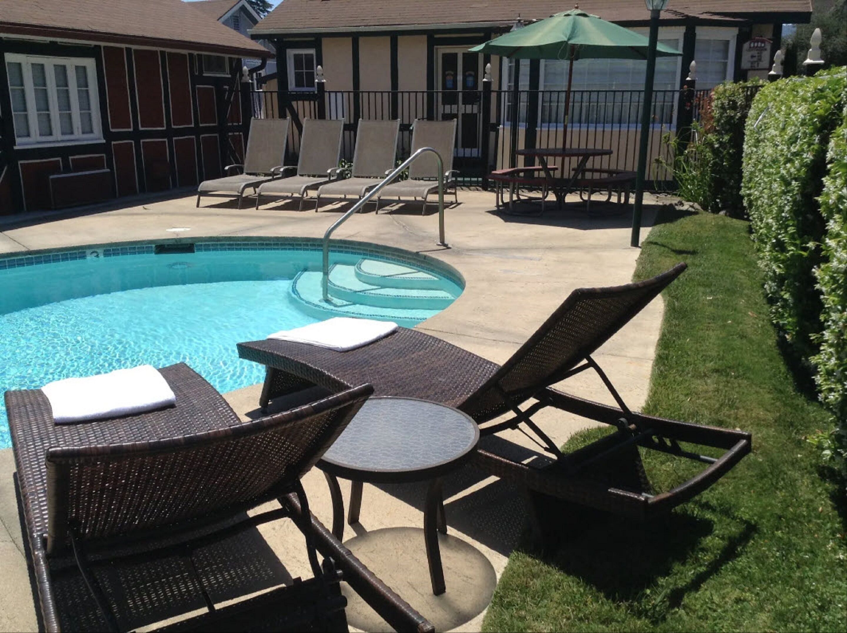 A pool area with lounge chairs and a small table, surrounded by a well-maintained lawn and a building in the background.