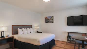 A hotel room with a large bed, bedside lamps, a flat-screen TV, a desk with a chair, and a painting on the wall.