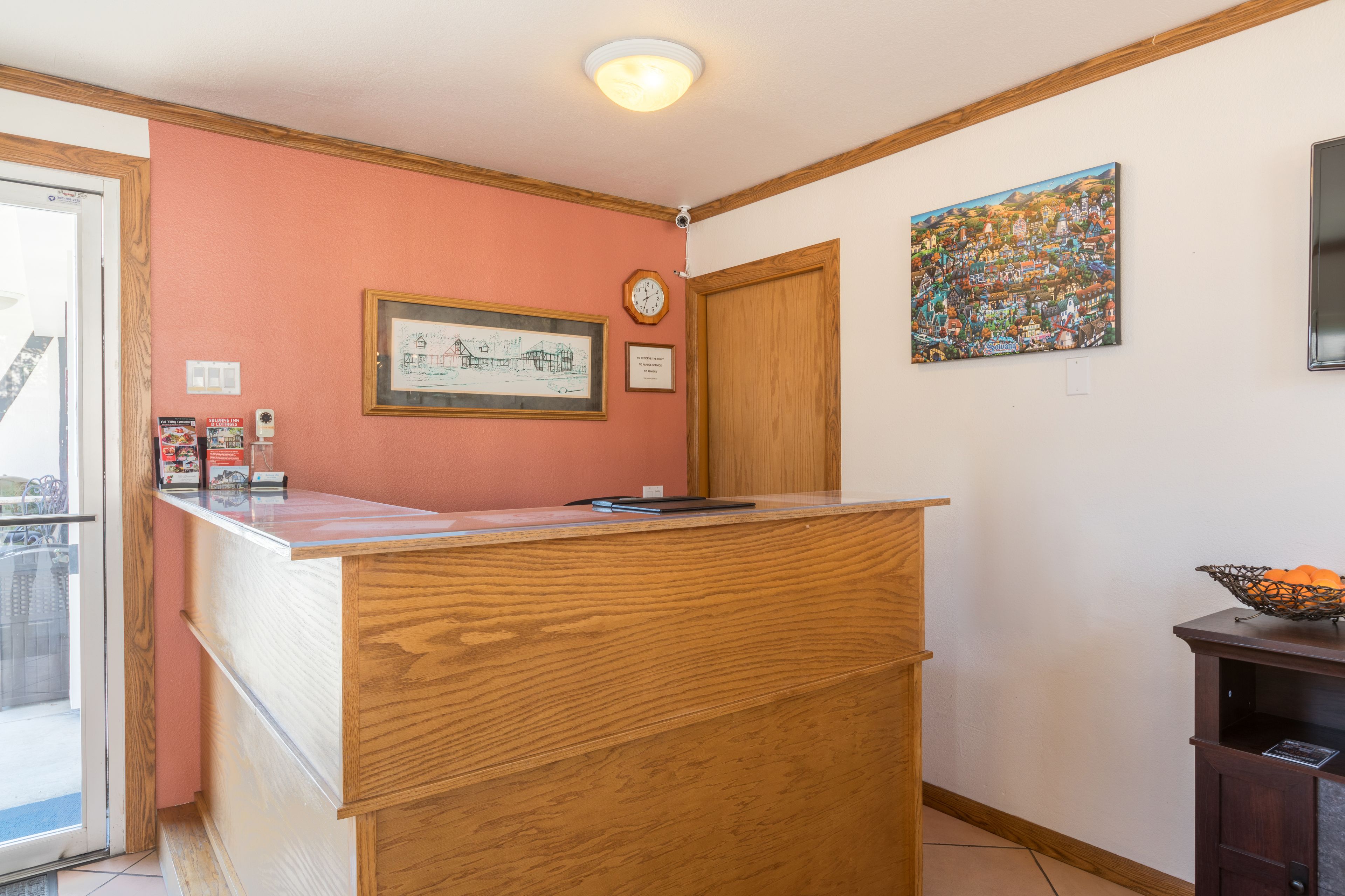 A reception area with a wooden counter, framed artwork, a clock, and a colorful painting on the wall.
