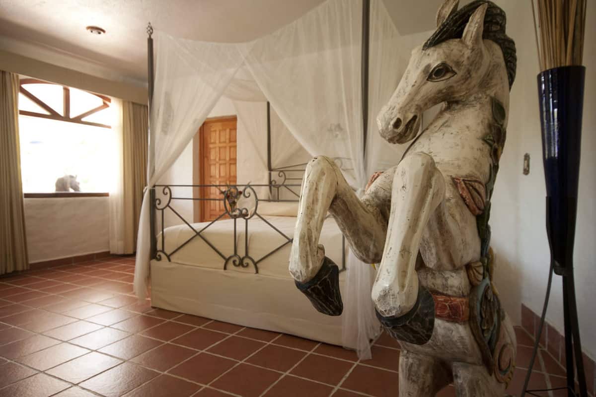 Une pièce comprenant un lit, une sculpture de cheval, une fenêtre avec des rideaux et une porte.