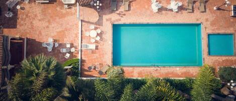 An aerial view of a swimming pool with tiled decking, lounge chairs, and a hot tub.