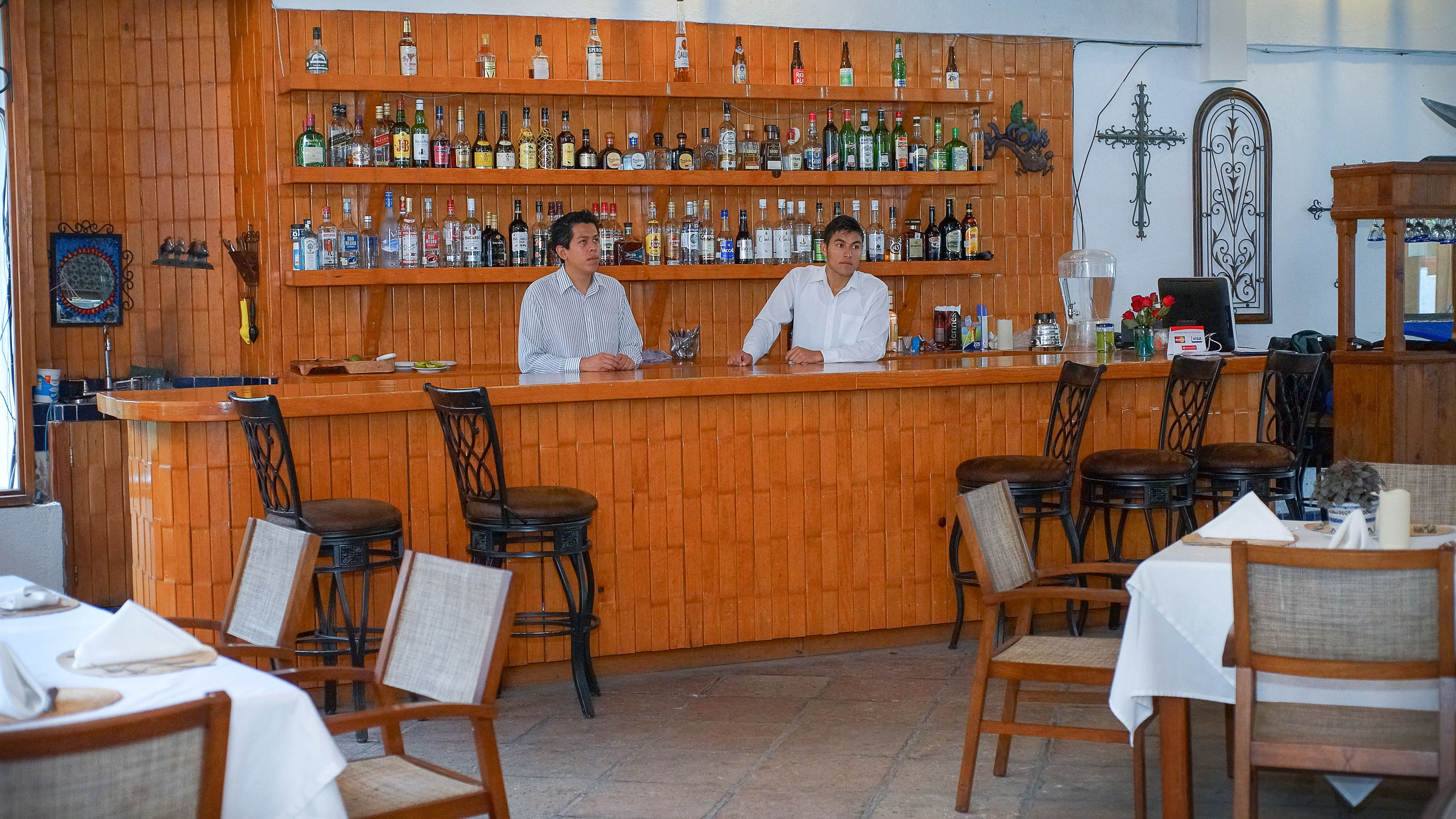 Un espace bar avec des panneaux de bois et une variété de bouteilles d’alcool. On y trouve des tabourets de bar et des tables avec des chaises.