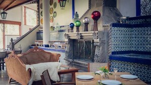 A dining area with a wooden table set for two, a sofa with a white throw, and a tiled wall with decorative plates. - Hotel El Rebozo (Valle de Bravo)