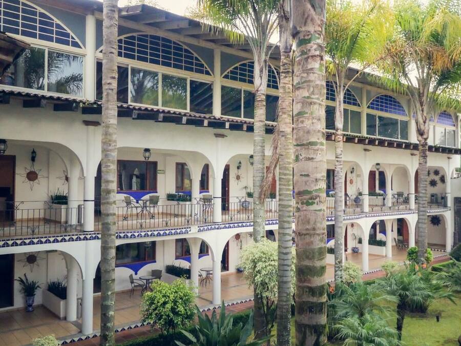 Un edificio de varios pisos con un patio central, que cuenta con balcones, arcos y plantas en macetas.