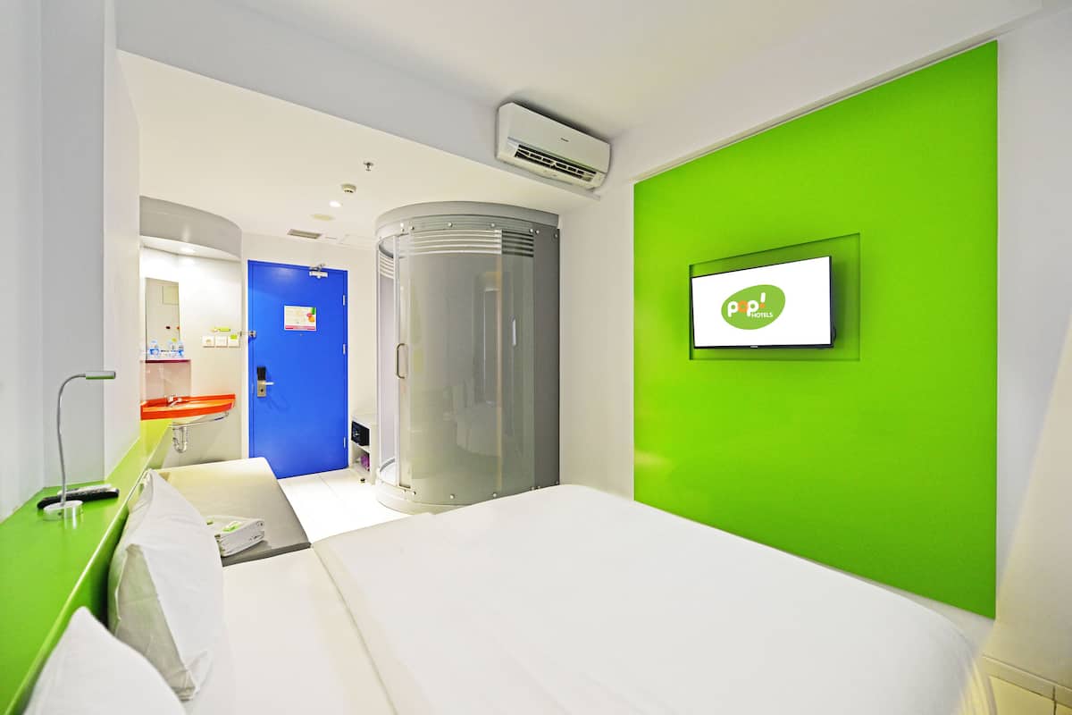 Een hotelkamer met een bed, een groene accentmuur, een televisie en een badkamer met wastafel en spiegel.