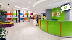 Un espace d’accueil d’hôtel avec un comptoir vert, un écran de télévision et un décor mural aux couleurs vives.