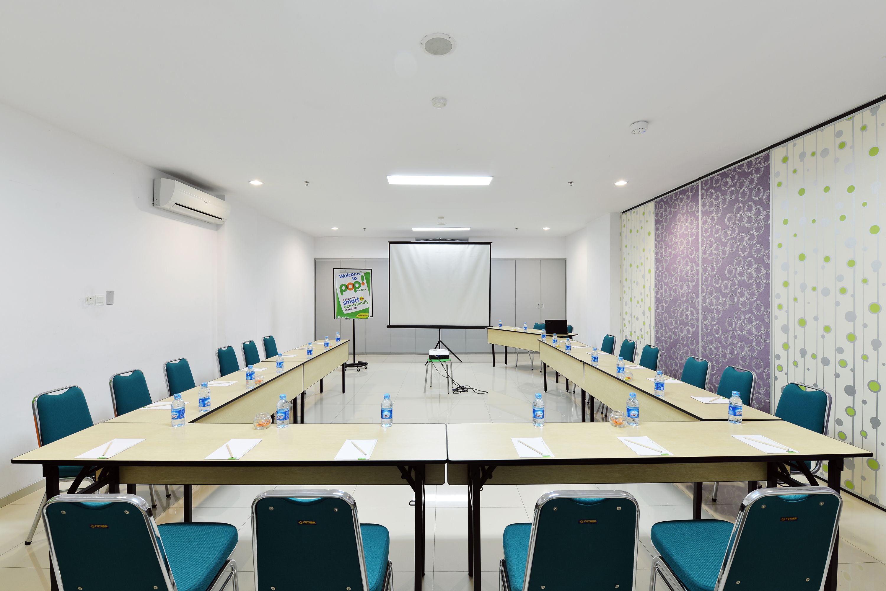 Uma sala de conferências com uma mesa comprida, cadeiras e uma tela de projetor.