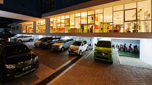 Un immeuble à plusieurs étages, avec un rez-de-chaussée bien éclairé et plusieurs voitures garées.