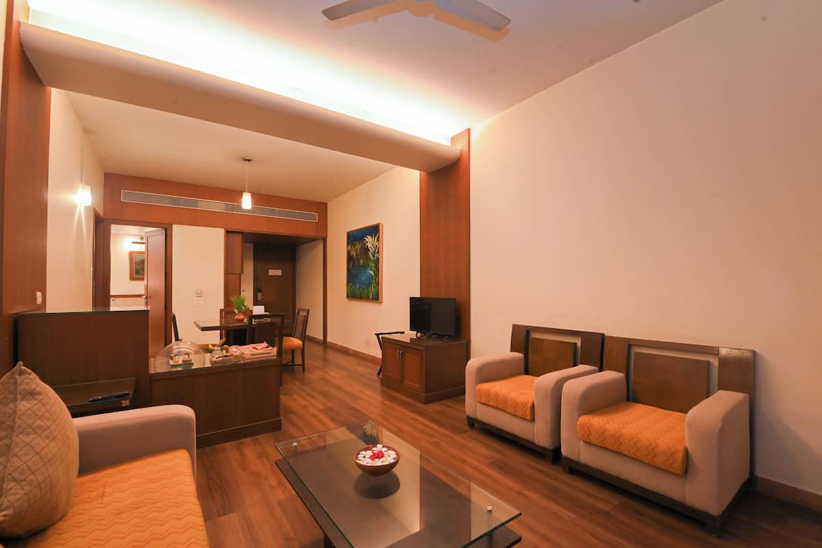 A hotel room with a seating area, a television, a small table with a bowl, and a painting on the wall.