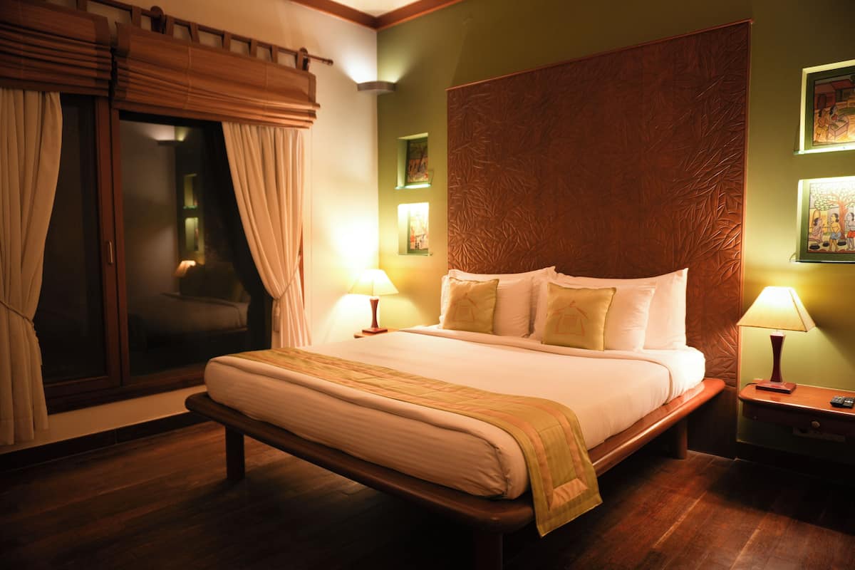A hotel room with a large bed, two bedside tables with lamps, a window with curtains, and a wooden headboard.