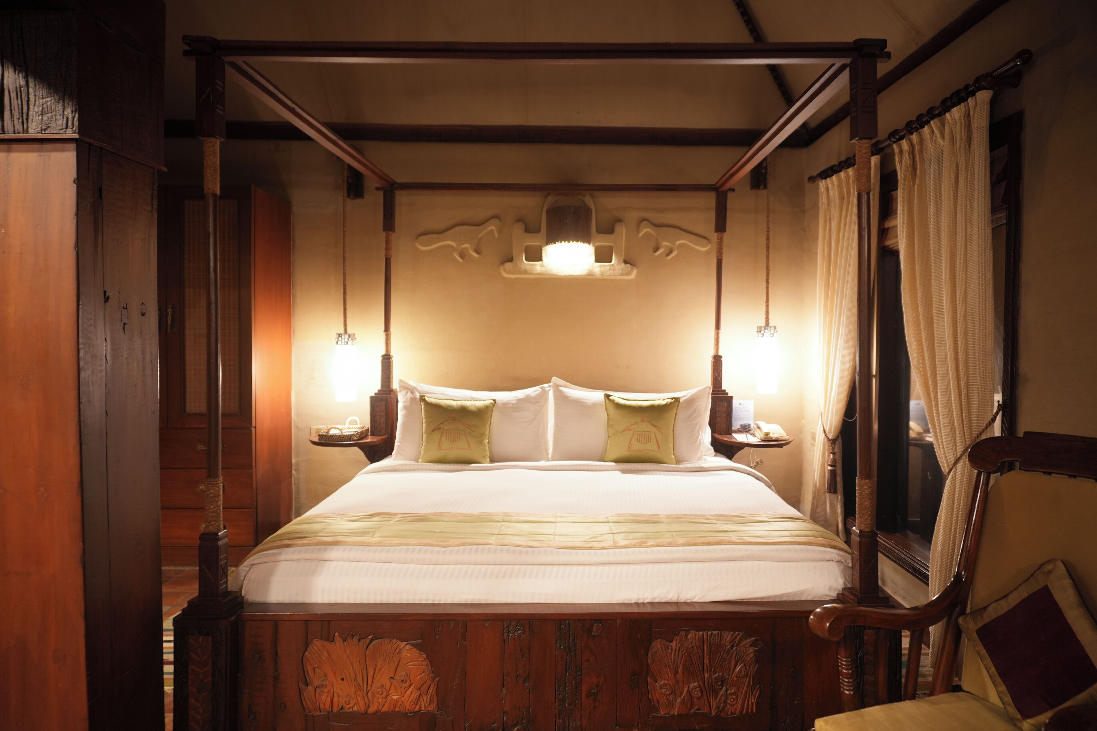 Een hemelbed met een baldakijn, een houten hoofdbord en twee nachtkastjes met lampen.