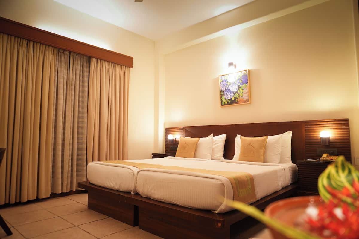 A hotel room with a double bed, a nightstand with a lamp, a painting on the wall, and a large window with curtains.