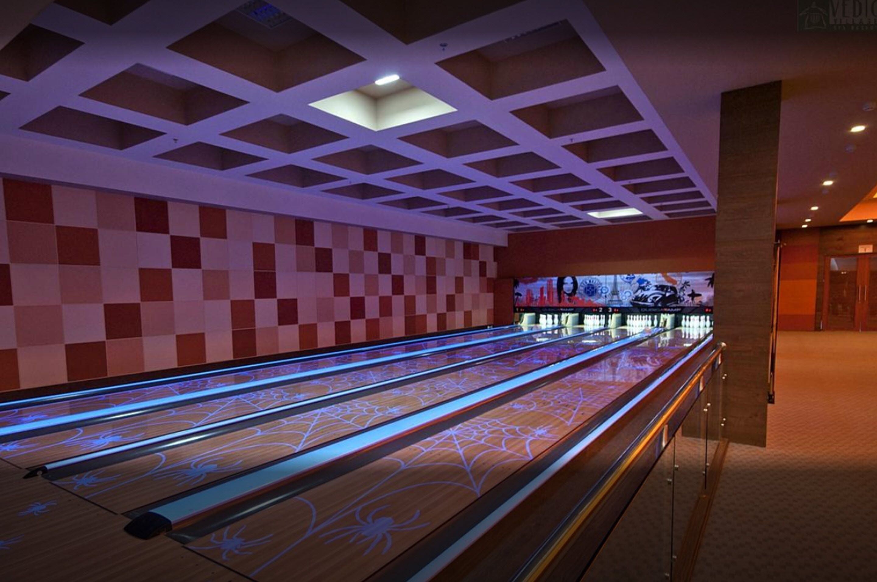 A bowling alley with a checkered wall and illuminated lanes.